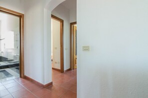 Un pasillo con suelo de baldosas, puertas de madera y un interruptor de luz en la pared.
