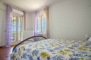Un dormitorio con cama, una silla, un aparador y una ventana con cortinas.