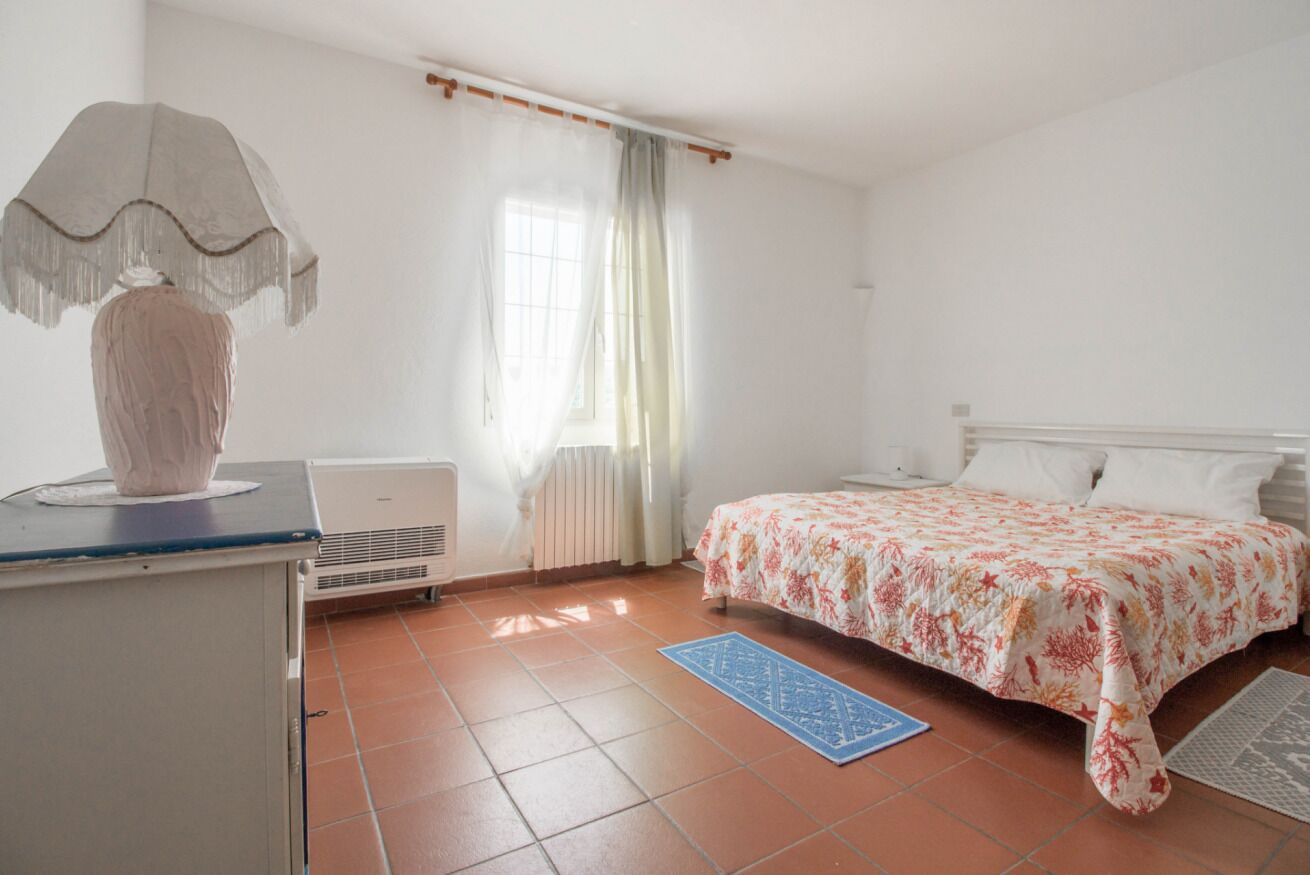 A bedroom with a bed, a desk, a lamp, a radiator, and a window with curtains.