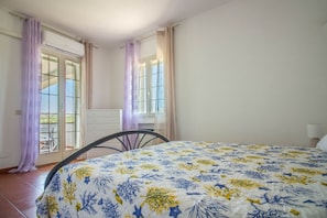 A bedroom with a bed, a chair, a dresser, and a window with curtains. - GuestHost - Cozy Apartment by the Vineyard (Arzachena)