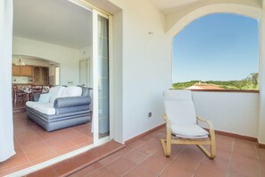 A balcony with a white chair, a sofa, and a view of greenery. - GuestHost - Cozy Apartment by the Vineyard (Arzachena)