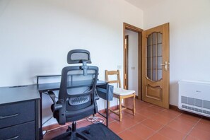 Une pièce comprenant un bureau, un fauteuil de bureau noir, une chaise en bois, une porte en bois et un climatiseur blanc.