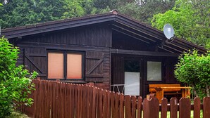 A wooden cabin with a satellite dish, a wooden deck, and a fenced yard.