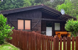 Eine Holzhütte mit Satellitenschüssel, einer Holzterrasse und einem eingezäunten Hof.