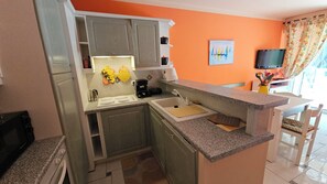 A compact kitchen with a sink, stove, and cabinets, a dining area with a table and chairs, and a television in the corner. - Apartment Gioia: Your Beachfront Paradise with Pool (Saint Raphael)
