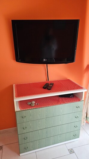 A television mounted on a wall, a green storage unit with drawers, and a red cushion on top. - Apartment Gioia: Your Beachfront Paradise with Pool (Saint Raphael)