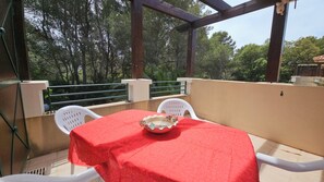 A balcony with a table covered in a red tablecloth, two white chairs, and a decorative bowl. - Apartment Gioia: Your Beachfront Paradise with Pool (Saint Raphael)