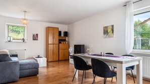 En moderne stue med en grå sofa, et spisebord med stole, et træskab og et fjernsyn.