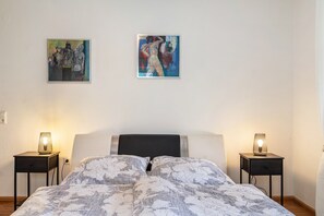 Ein Schlafzimmer mit einem Bett, zwei Nachttischen, zwei Wandlampen und zwei gerahmten Bildern.