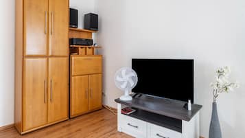 A room with a wooden wardrobe, a flat-screen TV, a white fan, and a vase with flowers.