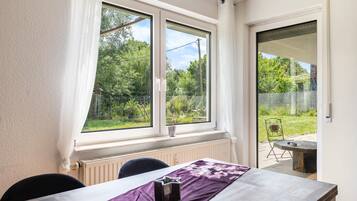 A room with a table, chairs, a window with a view of greenery, and a door leading outside.