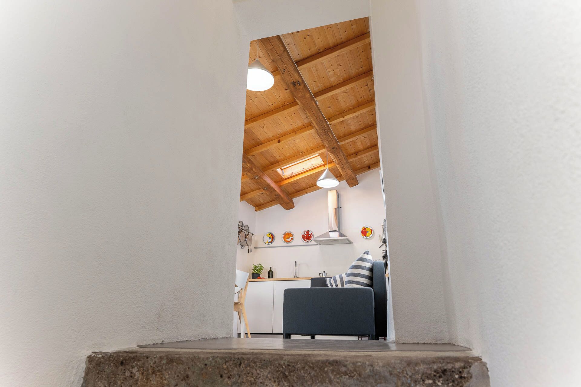 Una cocina moderna con vigas de madera, un área de comedor con un sofá y una pequeña mesa.