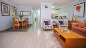 Uma sala de estar com área de jantar, cozinha ao fundo, um sofá e uma mesa de centro.