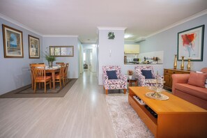 A living room with a dining area, a kitchen in the background, a sofa, and a coffee table. - Stylish Homebush Stay | Balcony, Parking, Sleeps 6 (Homebush West)