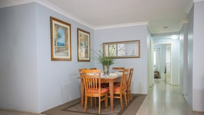 Uma sala de jantar com mesa e cadeiras, quadros nas paredes e um corredor que dá para outro cômodo.