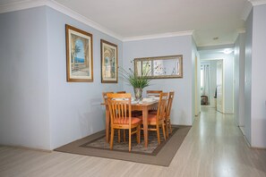 A dining area with a table and chairs, framed pictures on the walls, and a hallway leading to another room. - Stylish Homebush Stay | Balcony, Parking, Sleeps 6 (Homebush West)
