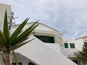 A white building with green shutters, a palm tree, and a clear sky. - Apartamento La Concha an Strand und Meer No 4 by Interhome (Corralejo)