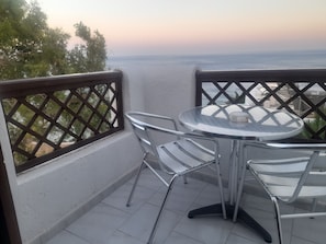 Ein Balkon mit einem runden Tisch und zwei Stühlen, mit Blick auf ein Gewässer.