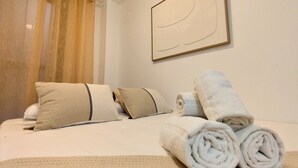 Een net opgemaakt bed met opgerolde handdoeken, kussens en een dekbed.