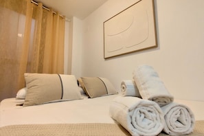 Una cama bien hecha con toallas enrolladas, almohadas y una manta.