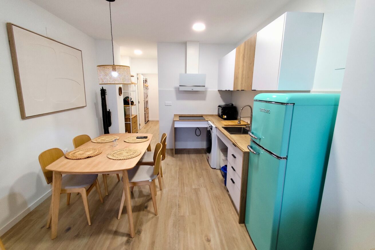 A compact kitchen with a dining area, a blue refrigerator, and a hanging light fixture.