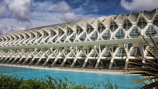 Een modern architectonisch gebouw met een opvallende, golfachtige dakconstructie en een zwembad op de voorgrond.