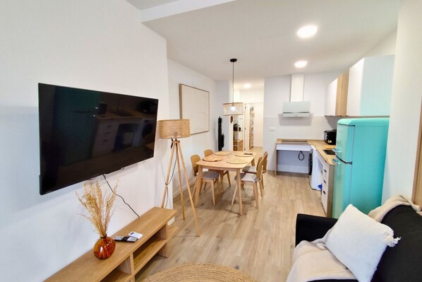 Una sala de estar moderna con televisor de pantalla plana, muebles de madera, comedor y pequeña cocina.