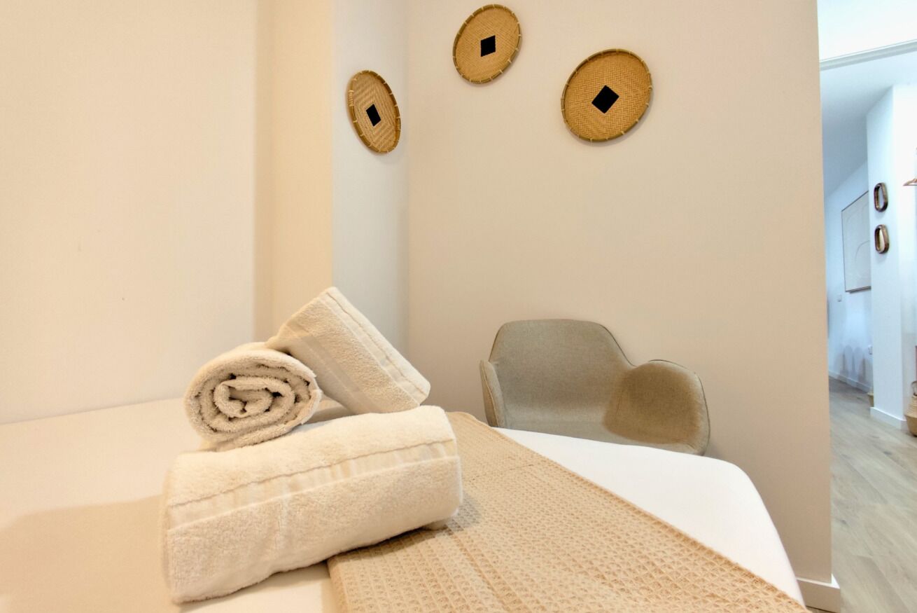 Un lit bien fait, avec des serviettes pliées en rouleaux, une chaise et trois éléments de décoration tissés accrochés au mur.