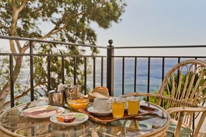 Une table en verre, sur laquelle sont disposés des aliments et des boissons pour le petit-déjeuner, se trouve sur un balcon donnant sur la mer.