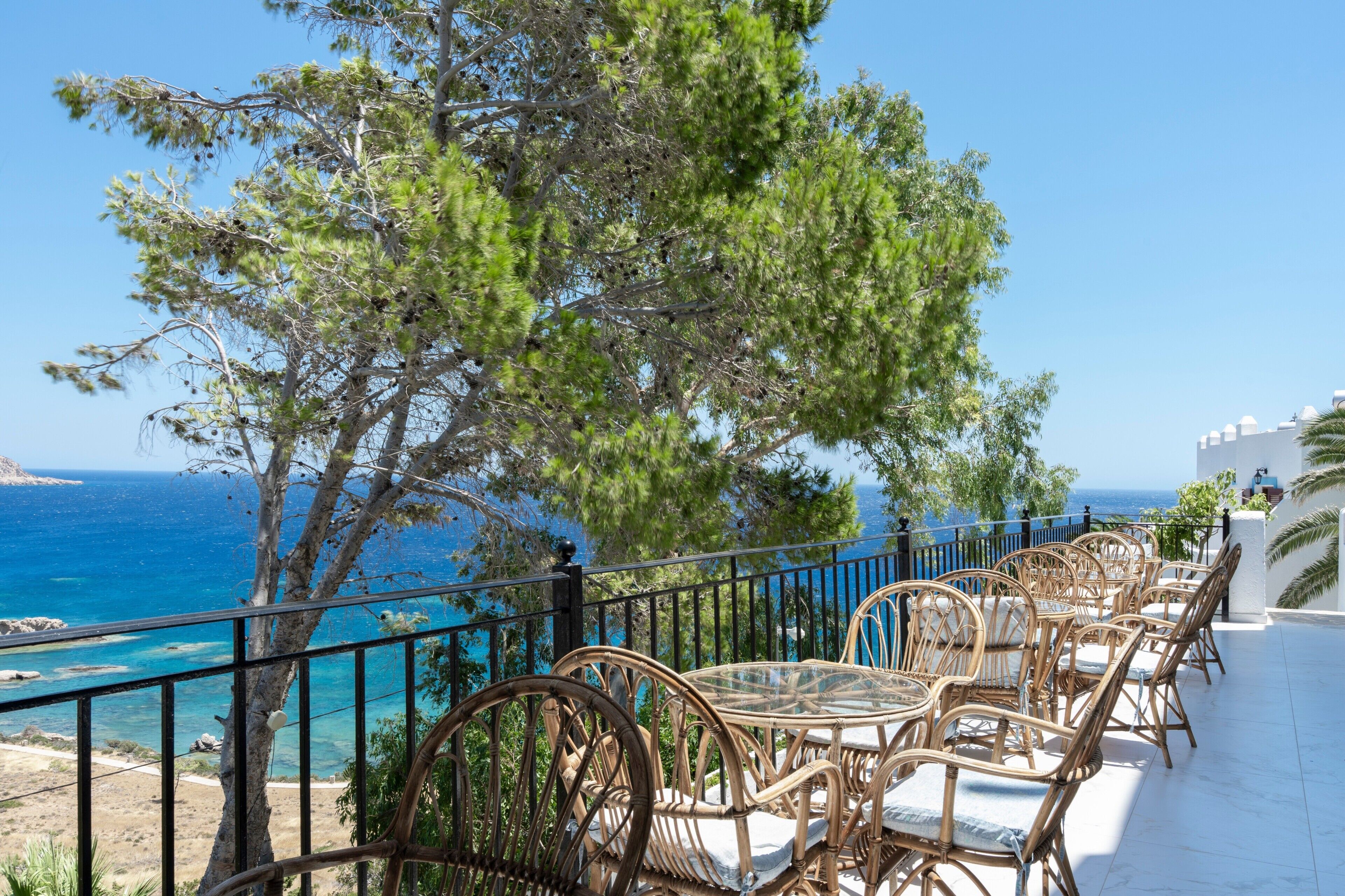 Terraza frente al mar con mobiliario de mimbre, con vistas al océano y a una costa rocosa.