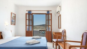 Habitación de hotel con cama, escritorio, silla y vista a un paisaje por una puerta abierta.
