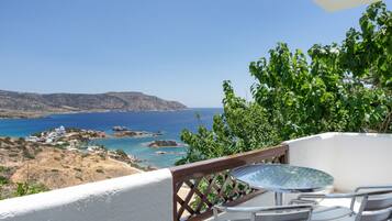 Un balcon avec une table et des chaises donnant sur un paysage côtier caractérisé par un terrain rocheux et une mer d’un bleu limpide.