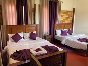 Hotellihuone, jossa on kaksi sänkyä, puiset päätyosat ja violetit vuodevaatteet.