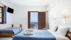 Habitación de hotel con dos camas, televisión, puerta que da a un balcón con vista al mar y una silla.