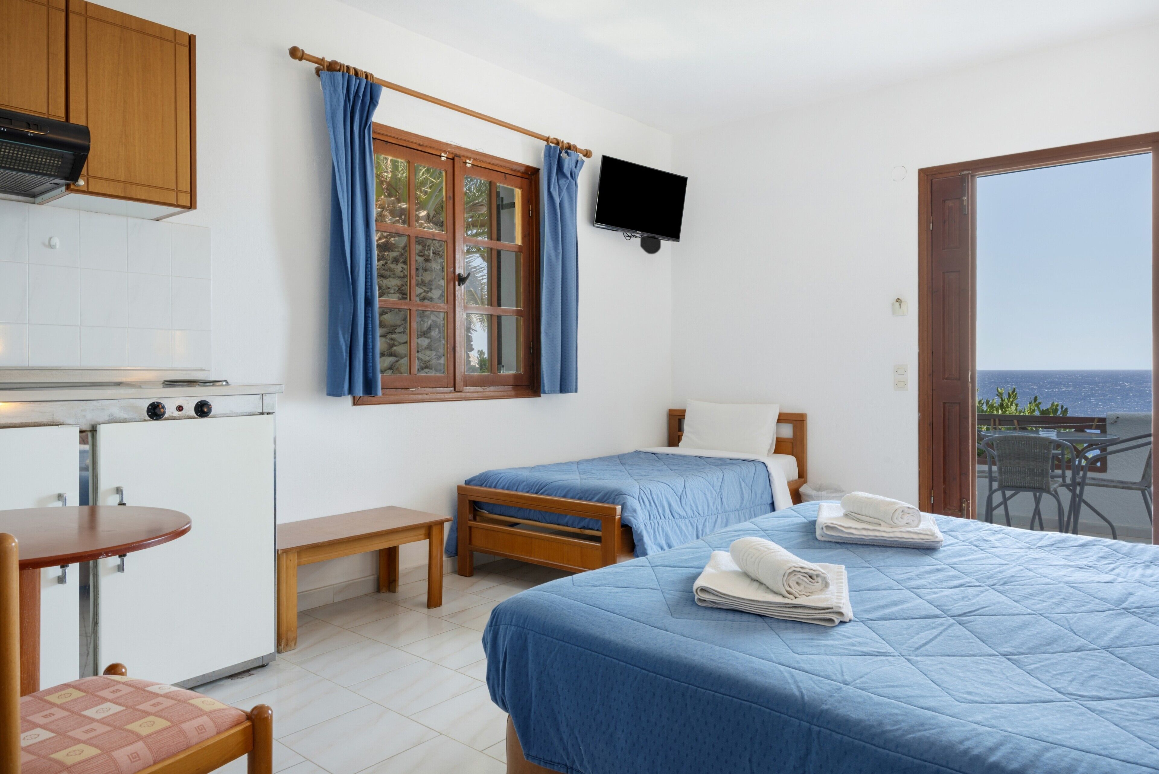 Una habitación con dos camas, una kitchenette pequeña, televisor y balcón con vistas.