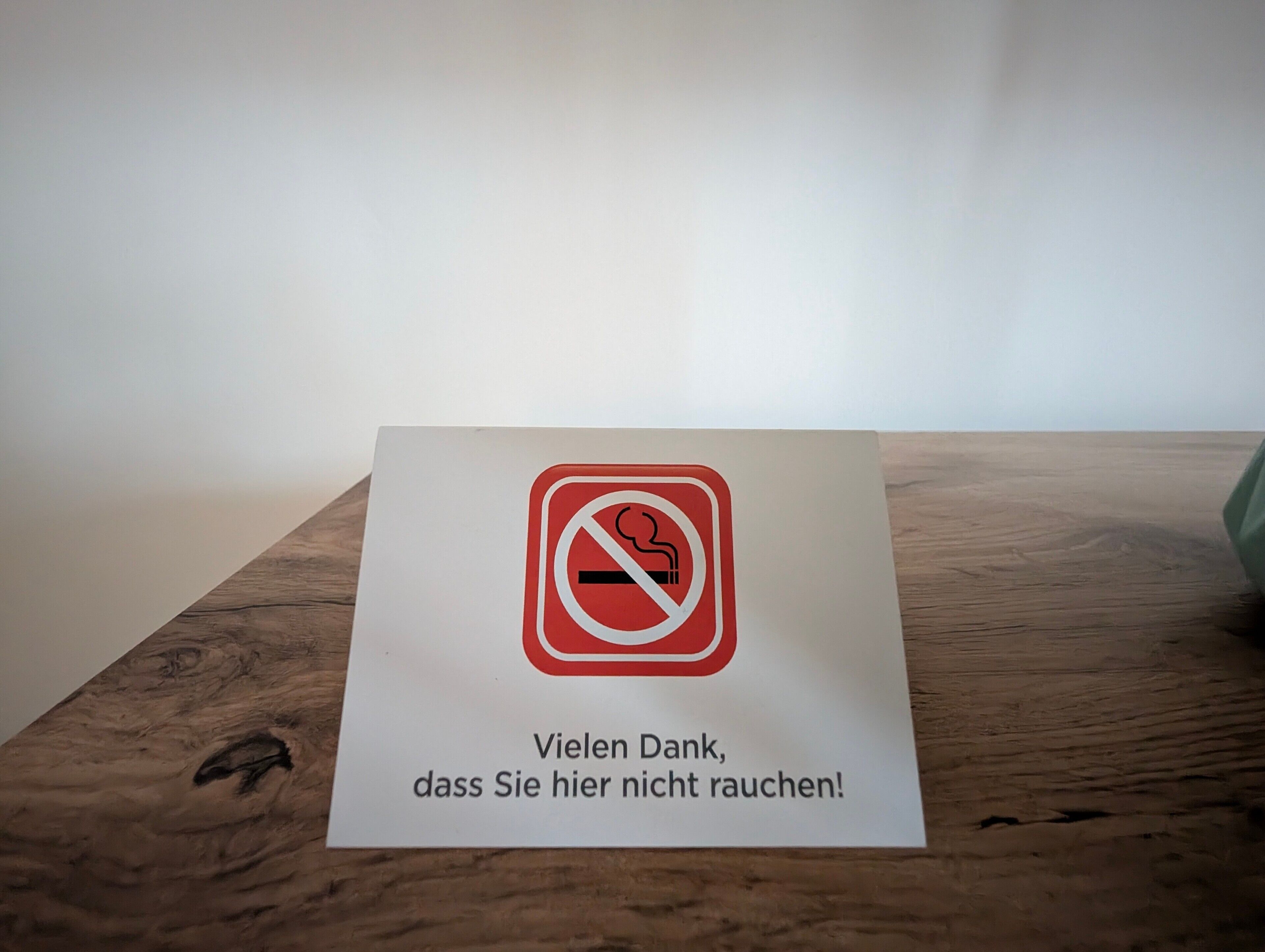 Un panneau «interdiction de fumer» avec un message en allemand, placé sur une surface en bois.