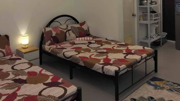 Quarto com duas camas, uma mesa de cabeceira com abajur, um quadro na parede e uma estante com objetos.