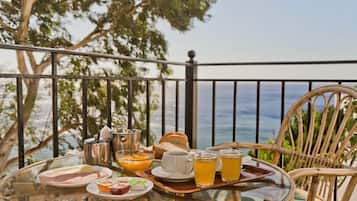Une table en verre, sur laquelle sont disposés des aliments et des boissons pour le petit-déjeuner, se trouve sur un balcon donnant sur la mer.