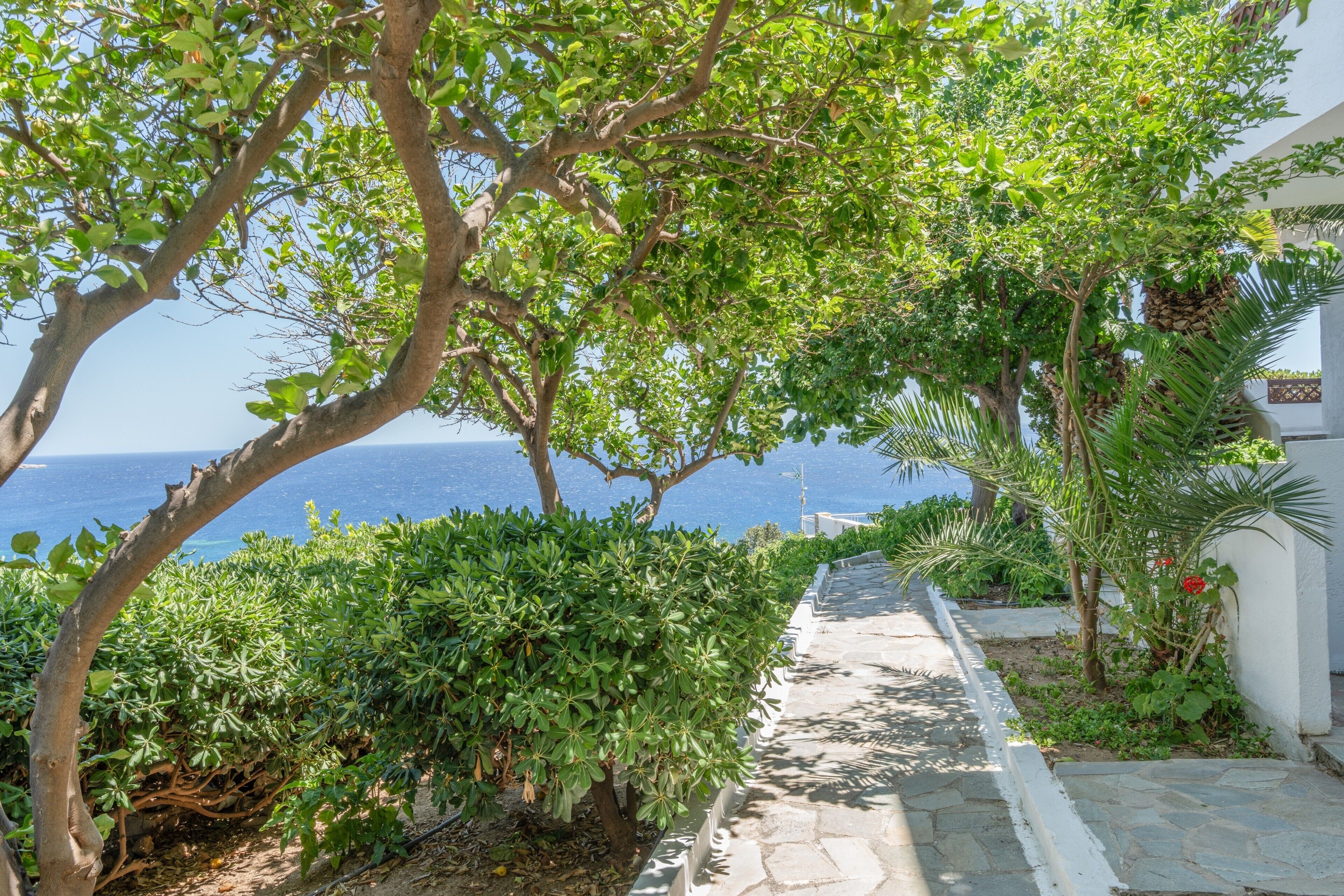 Un chemin de pierre mène à un bâtiment blanc d’où l’on a vue sur la mer.