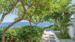 Un chemin de pierre mène à un bâtiment blanc d’où l’on a vue sur la mer.