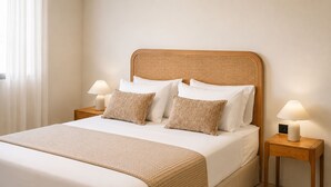 Un letto ben rifatto con testiera in rattan, due comodini con lampade e un'ampia finestra con tende leggere.