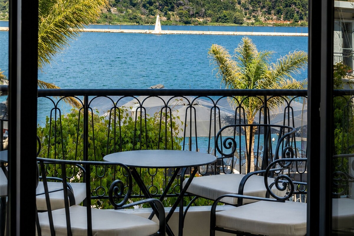 Ein Balkon mit Tisch und Stühlen, der auf ein Gewässer und eine hügelige Landschaft blickt.
