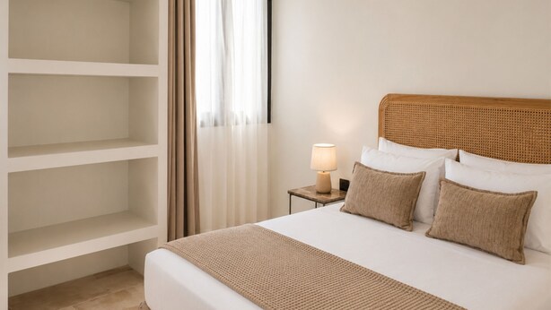 Una camera d'albergo con un letto, un comodino con una lampada, un armadio e una finestra con tende.