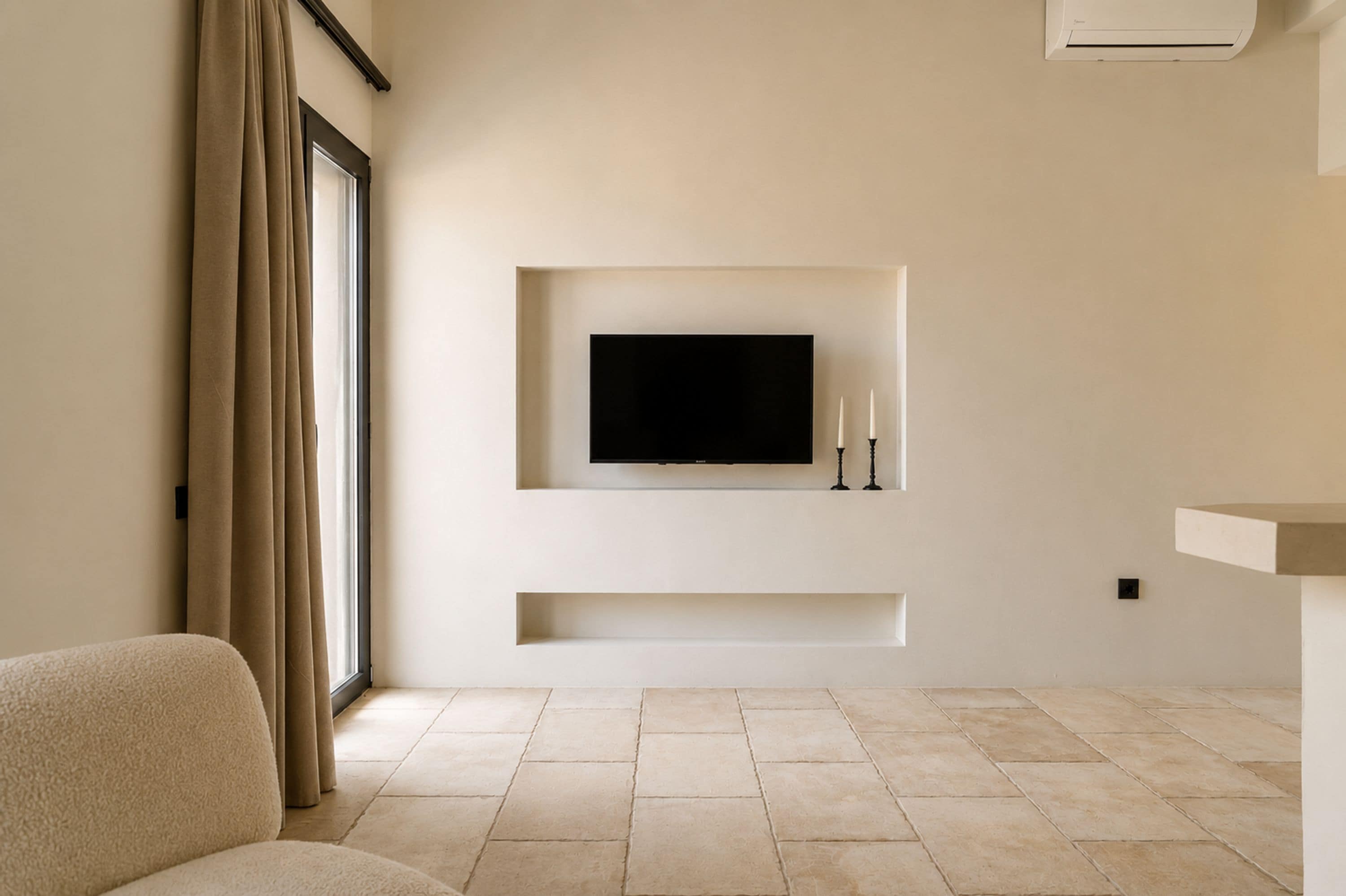 Uma sala de estar moderna com uma televisão de tela plana na parede, um sofá e uma janela grande com cortinas.