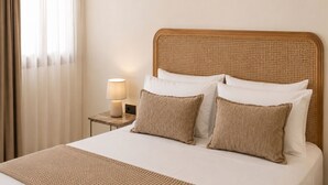Un letto con testiera intrecciata, due cuscini, una lampada da comodino e una coperta con trama.
