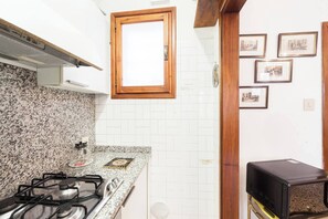 A kitchen with granite countertops, a gas stove, a microwave, and a small refrigerator. - Campiello Chiesa, Venice By Short Holidays (Venice)