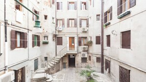 A narrow courtyard with a central staircase leading to an upper floor, surrounded by buildings with multiple windows and balconies. - Campiello Chiesa, Venezia (Venice)