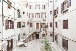 A narrow courtyard with a central staircase leading to an upper floor, surrounded by buildings with multiple windows and balconies. - Campiello Chiesa, Venezia (Venice)