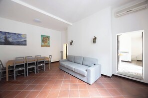 Ein Wohnzimmer mit einer Couch, einem Esstisch mit Stühlen, einem Bild an der Wand und einer Tür zu einem anderen Raum.