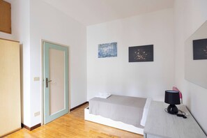 A bedroom with a bed, a desk with a lamp, a door, and two wall-mounted paintings.